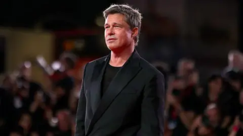 Getty Images Brad Pitt standing in front of a blurred crowd, wearing a black suit jacket and black tshirt