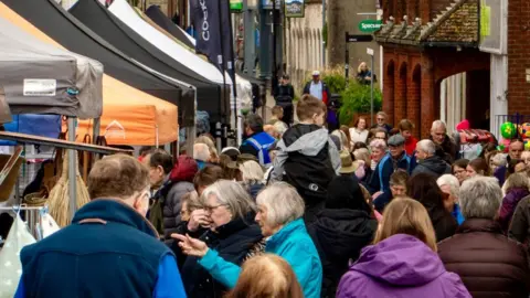 Crowds of people looking at a row of stalls covered by gazebos