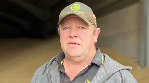 Dan Willis is wearing a black T-shirt, grey hoodie and a black cap that says John Deere on it.