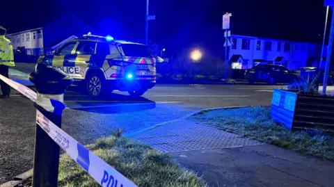 A police car is parked on a quiet street. An officer is standing next to it.