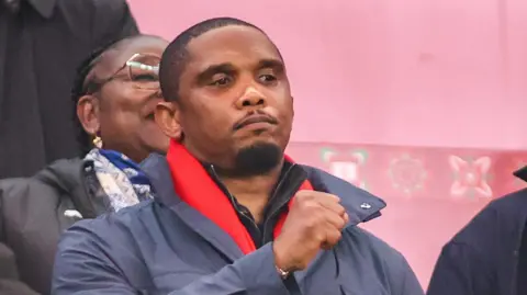 Samuel Eto'o raises his right fist while seen in the stands at a football match