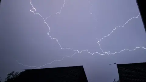 Lightning streaks across the sky above houses during a thunderstorm in June 2025