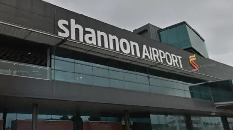 the glass fronted exterior of Shannon Airport, with a sign showing the airports name and logo 