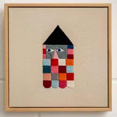 Stewart Francis Easton A stitched piece of art comprises colourful squares with a black peak. Two eyes and a nose can also been seen in the piece. 