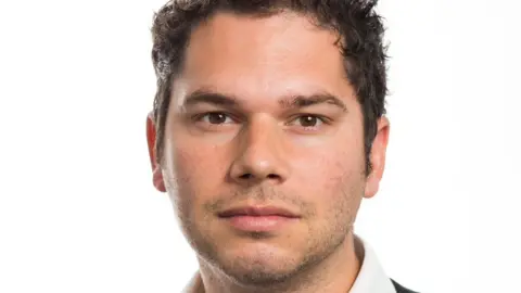 Howard League for Penal Reform Robert Preece with short dark hair and slight stubble looking at the camera while wearing a shirt with a white collar.