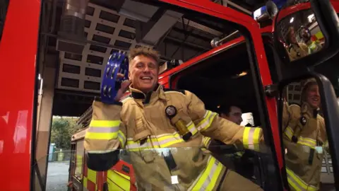 South Yorkshire Fire and Rescue A firefighter leans out an engine and shakes a tambourine.