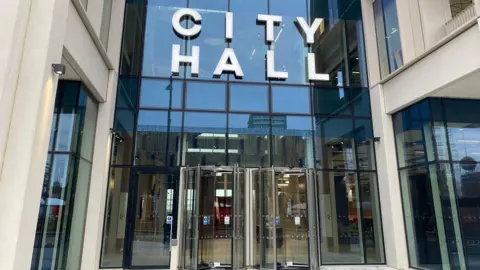 Sunderland City Council's headquarters. The glass fronted building has two revolving doors at its entrance. The words CITY HALL sit above the doors.