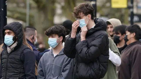 PA Media Three students wearing blue face masks among a crowd of people 