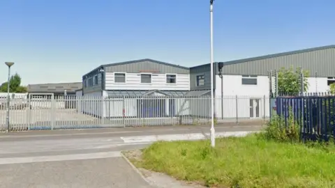 Impression of a warehouse building behind a steel fence