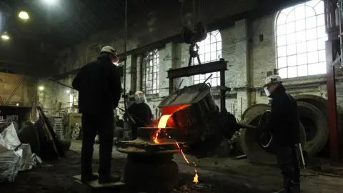 Charnwood Borough Council Three workmen in protective clothing pour molten metal into a bell casting case