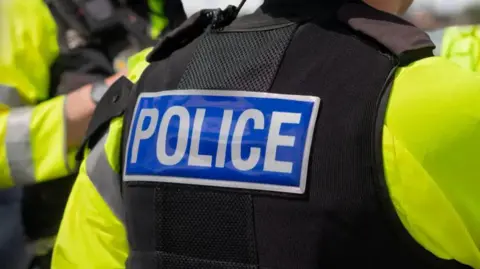 The back of a person wearing a black police vest with the word POLICE written in white on a blue background