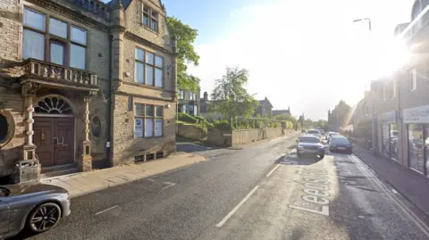 Google A single carriageway high street with a decorative building on the left and a Tesco Express on the right.