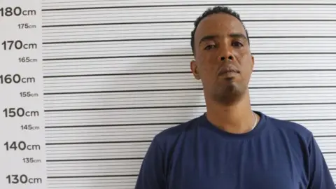 Mohammed Tahir aka "Wordi" in a navy T-shirt stands against a measuring chart in a police photo - putting his height at around 178cm.