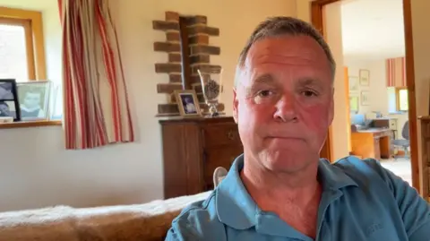 Andrew Turner/BBC Simon Lush, sitting in his living room