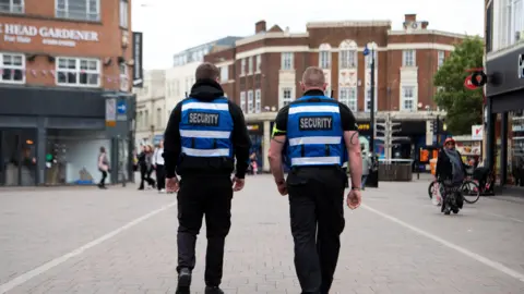 Charnwood Borough Council The backs of two street security staff wearing blue and black uniforms