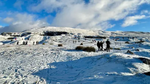 Lucy O | BBC Weather Watchers People sledging and walking on a snowy hillside in the sunshine
