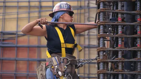 Woman in hard hat is attached to metal railing while working