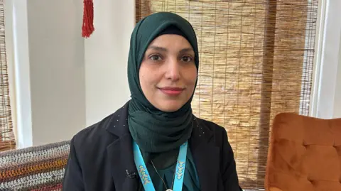 A woman from Syria wearing a black jacket and a dark green hijab.