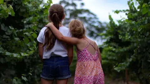 Photo of the backs of two small girls hugging each other. They are standing outside. 