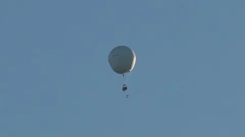 Brian Abram A white gas balloon flying through a clear blue sky.