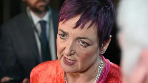 Getty Images Angela Constance, who has short purple hair, in a close-up shot in a press huddle. She is wearing a red top and silver necklace. 