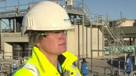 Nicola Shaw in a helmet and high vis jacket stood in front of a sewage works
