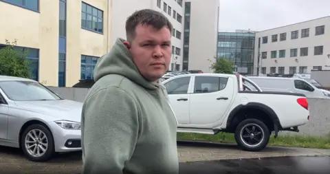 Jordan Willetts looks at the camera. He is wearing a green hoodie and has short dark hair. 