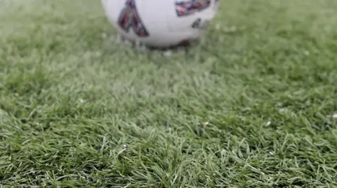 PA Media An artificial playing field with a football in the background.