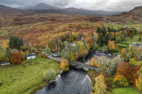 Bletheration/BBC Weather Watchers An aerial view of Bridge of Gaur showing an upland landscape of hills and, in the distance, mountains. A stone bridge spans a river and there is a two-storey white walled house among tree on the riverside.