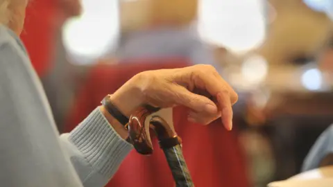 A stock image showing the hand of an elderly person perched on a walking stick. 