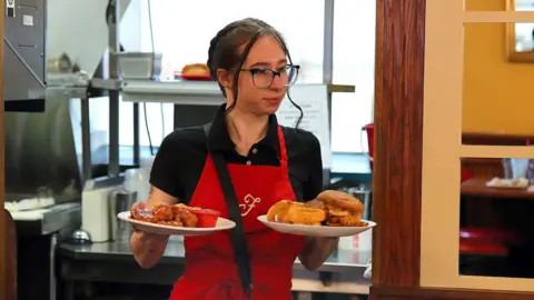 Getty Images A waitress in the US wearing a red apron with the letter F on the front, bringing out two plates of food