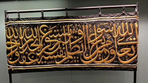 Amanda White/BBC A black cloth embroidered with gold lettering hanging from a metal display rail.