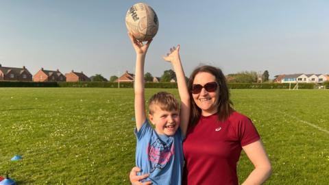 Mum and son playing rugby on an open field on a sunny day