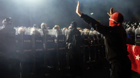 Getty Images A protester in Istanbul holds their hands up to a line of riot police.