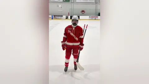 James Dawson Rufus Dawson on the ice in Sherbrooke, Quebec, in December 25 for an All Stars Showcase. Rufus is in all red and is holding two pucks. He is wearing black skates and a white helmet. The red kit has 'Stanstead' written diagonally on the front.