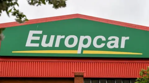 White lettering which says Europcar on a green background and over a yellow line, on a building.
