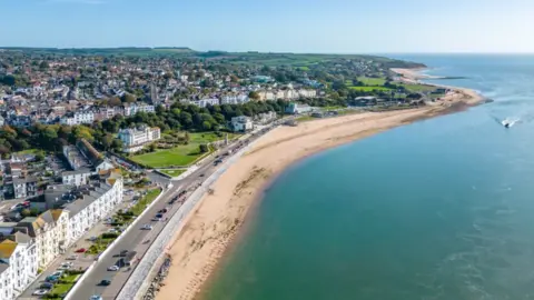 The sea is seen to the right, then a beach and then the homes and businesses of Exmouth to the left 