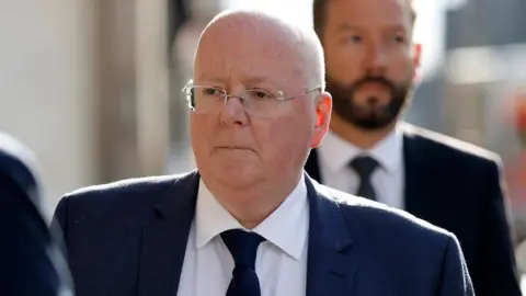 Peter Murrell, who is bald with glasses, in a close-up shot while walking outside. He is wearing a business suit 