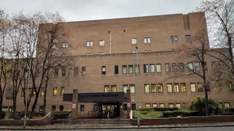 A court building made of brown brick. There are trees with no leaves on them in front of the building.