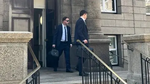 BBC A man wearing a suit and sunglasses exiting the Royal Court.