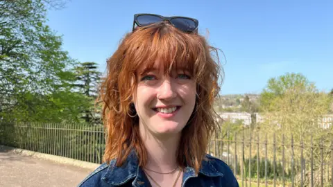 A young woman with brunette hair and blue eyes with sunglasses on her head