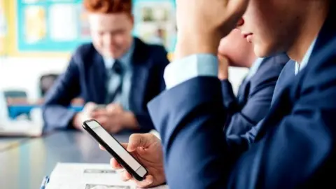 Getty Images Anonymous students in a classroom staring at their cell phone screens