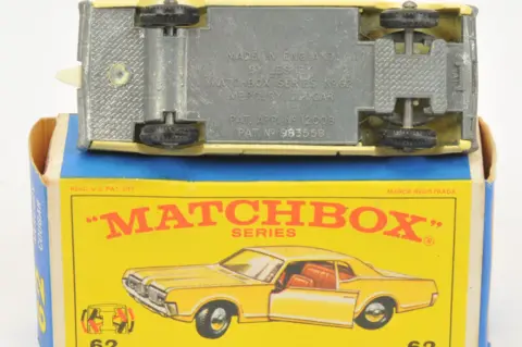 Vectis The yellow car is put on its side so you can see the underside which is grey. It is sitting on top of the yellow and blue box which has the words "Matchbox" written in red with a picture of the yellow car.