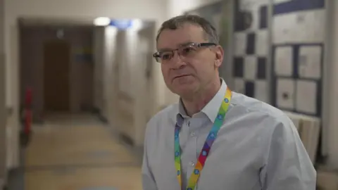 David French a man with glasses and a multi-coloured lanyard stood in a hospital ward.