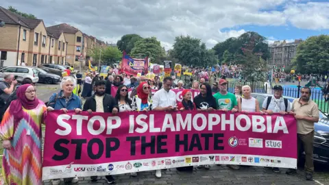 Hundreds of anti-racism campaigners marching behind a huge banner that says Stop Islamaphobia Stop the Hate