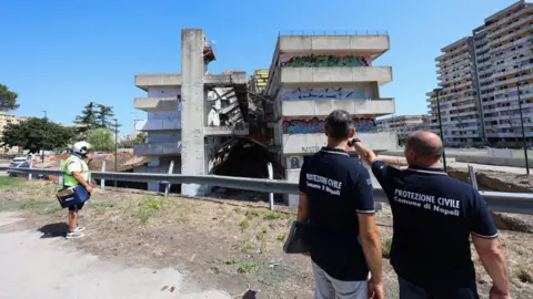 Marco Cantile/LightRocket Twee mannen van de Civiele Bescherming voor een gebouw in de wijk Scampia in Napels