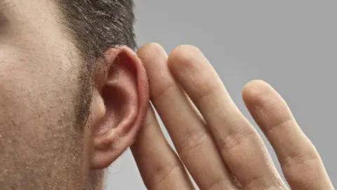 A close up of a man holding his left hand up to his left ear