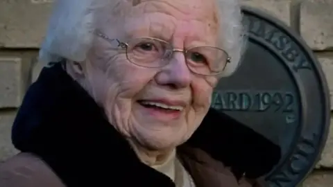 Brenda Fisher. She is standing in front of a plaque. 