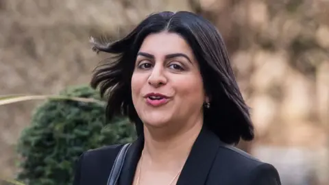 Justice Secretary Shabana Mahmood, wearing a black blazer and gold jewellery, walking towards Downing Street