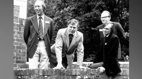 Sussex Wildlife Trust Sir David Attenborough pictured with Frank Penfold, Robin Crane and David Streeter at the opening of Sussex Wildlife Trust's Woods Mill Countryside Centre near Henfield in 1981. Sir David is leaning both his hands on a stone bridge. 